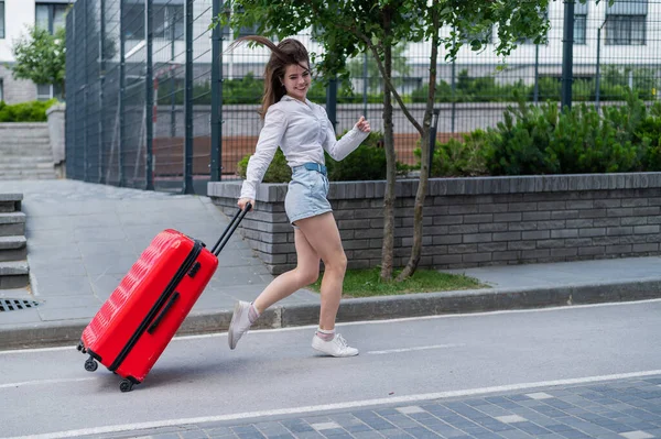 Glücklich schöne kaukasische Frau läuft mit einem großen roten Koffer nach draußen. Aufgeregtes Mädchen kommt zu spät ins Flugzeug. — Stockfoto