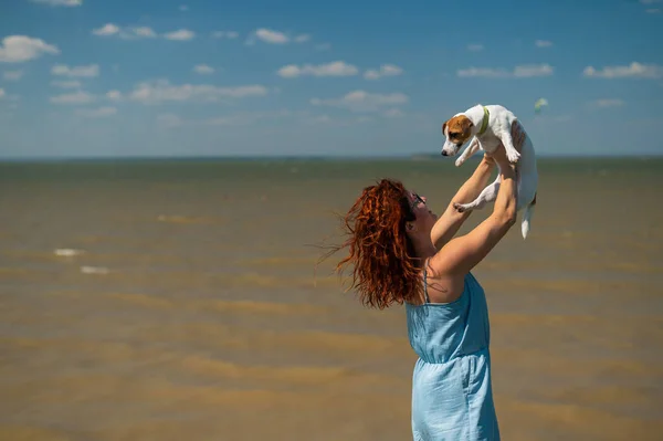Счастливая женщина обнимается с собакой у моря. Рыжая белая девушка держит щенка Джека Рассела Терьера — стоковое фото