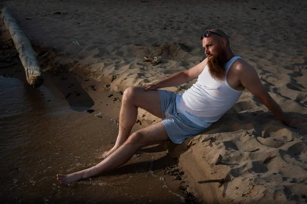 Divertente uomo calvo con la barba rossa vestita in biancheria intima in posa sulla spiaggia. Una parodia maschile divertente di una ragazza glamour. — Foto Stock
