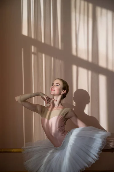 美しい優雅なバレリーナは、窓の背景を背景にホールで練習しています。チュチュのスレンダー女性とダンスクラスのポイントシューズ. — ストック写真