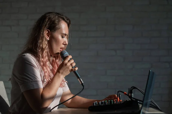 A woman sings into a microphone and plays online. A female blogger is recording a song using a synthesizer with a laptop.
