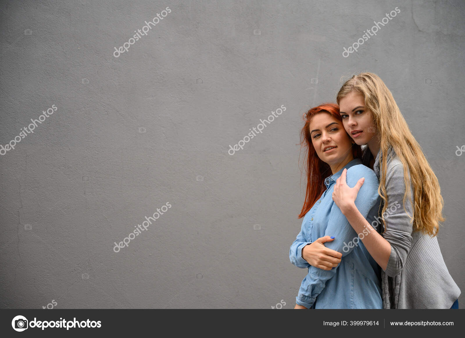 Two happy girlfriends are hugging on the background of a gray wall. Gentle hugs of a female lesbian couple