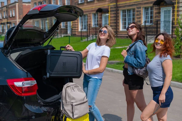 Drei Freunde gehen auf Roadtrip und laden ihre Koffer in den Kofferraum des Autos. — Stockfoto