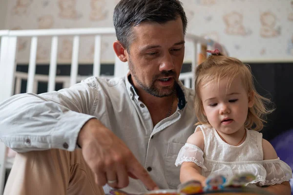 A caring father reads a fairy tale to his little daughter in the childrens bedroom.