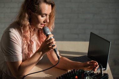 Bir kadın mikrofona şarkı söylüyor ve internetten çalıyor. Bir kadın blogcu dizüstü bilgisayarlı bir sentezleyici kullanarak şarkı kaydediyor..