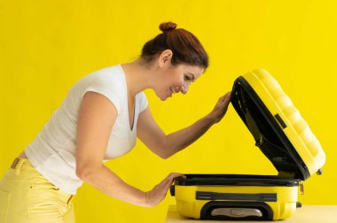 Beyaz kadın tatile çıkıyor ve sarı arka planda bavul hazırlıyor.