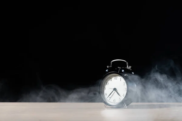 Reloj despertador clásico sobre la mesa en humo sobre fondo negro. —  Fotos de Stock