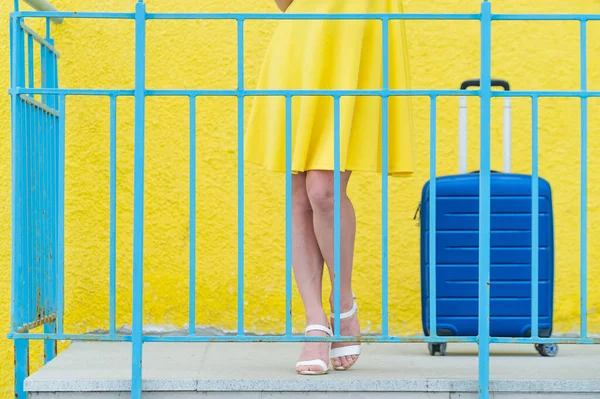 Ženské nohy v botách na vysokých podpatcích s modrým kufříkem na zábradlí boty na žlutém pozadí. — Stock fotografie