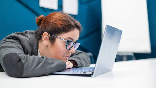 La femme d'affaires fatiguée posa la tête sur le bureau et regarde le moniteur de l'ordinateur portable. Une employée est fatiguée au travail au bureau. — Photo
