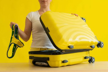 Yüzü olmayan kadın, sarı arka planda bir bavulda bikini katlıyor. Kız denize yolculuk için bavul hazırlıyor. Tatil.