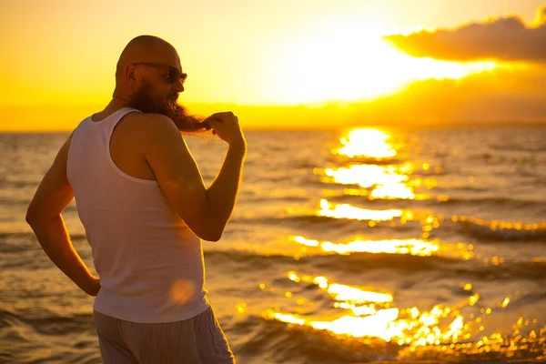 Un uomo calvo brutale posa sulla spiaggia al tramonto parodia pulcino glamour — Foto Stock