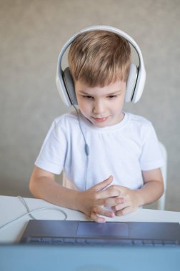 Kulaklıklı çalışkan bir çocuk bir masada oturur ve bir dizüstü bilgisayardan online ders izler..