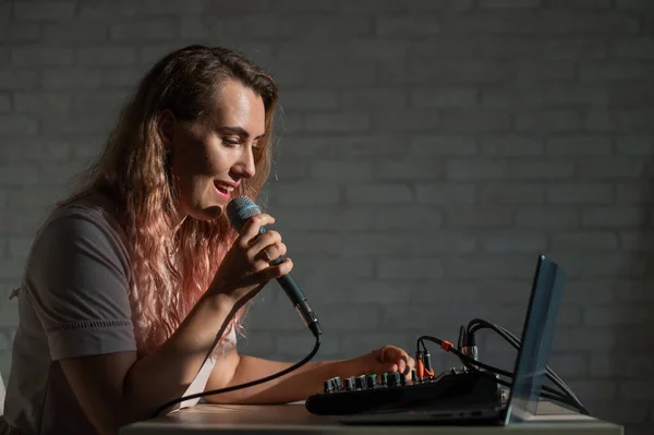 Eine Frau singt in ein Mikrofon und spielt online. Eine Bloggerin nimmt einen Song mit einem Synthesizer und einem Laptop auf. — Stockfoto