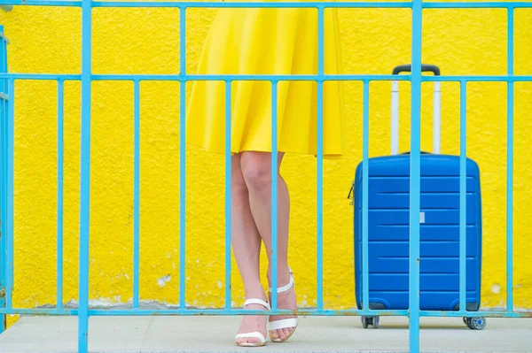 Vrouwelijke benen in schoenen met hoge hakken met een blauwe koffer voor schoeisel op een gele achtergrond. — Stockfoto