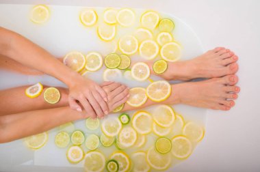 Meçhul, güzel bir kadın süt limonları ve limonla banyo yapıyor. Kesilmiş fotoğraf. Cilt beyazlatıcı banyoda kadın eli ve ayaklarının yakın çekimi.