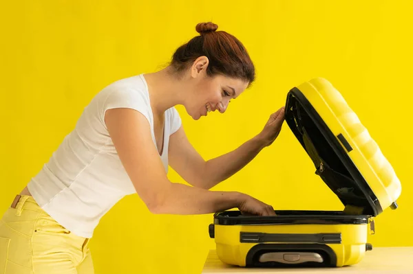 Mujer caucásica va de vacaciones y maleta de embalaje sobre fondo amarillo —  Fotos de Stock