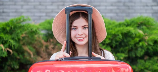戴着帽子的年轻美丽的高加索女人从一个有把手的红色行李箱里往外看。快乐的女孩带着行李去旅行.暑假的概念. — 图库照片