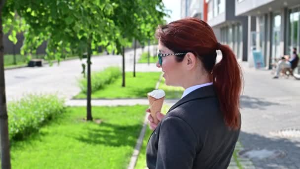 Uma mulher de fato de negócios vira-se e come um gelado de baunilha ao ar livre. . — Vídeo de Stock