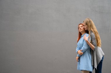 İki mutlu kız arkadaş gri bir duvarın arkasında sarılıyorlar. Lezbiyen bir bayana nazikçe sarılmak. LGBT Eşcinsel Evliliği.