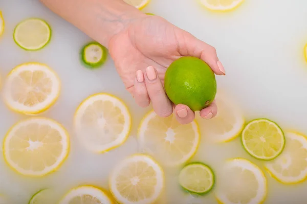Close-up of a female hand holding a lime over white water with lemon slices — Stock Photo, Image