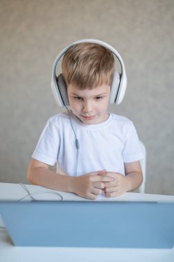 Kulaklıklı çalışkan bir çocuk bir masada oturur ve bir dizüstü bilgisayardan online ders izler..