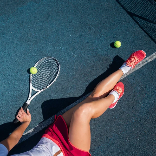 Uma menina sem rosto em uma saia esportiva se senta em um campo de tênis e segura um foguete. Visão superior das pernas femininas. — Fotografia de Stock