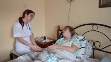 Bir doktor yaşlı bir kadın hastaya evde danışır. Terapist yaşlı bir kadını yatakta tedavi ediyor..