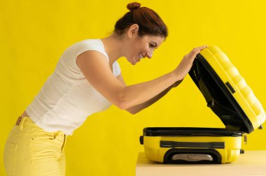 Beyaz kadın tatile çıkıyor ve sarı arka planda bavul hazırlıyor.