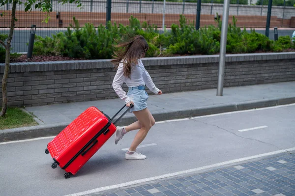 Gelukkig mooie blanke vrouw loopt met een grote rode koffer buiten. Opgewonden meisje is te laat voor het vliegtuig. — Stockfoto