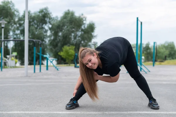 Grasso giovane donna che fa esercizi di stretching all'aperto. Ragazza in sovrappeso fa curve prima di fare jogging. — Foto Stock