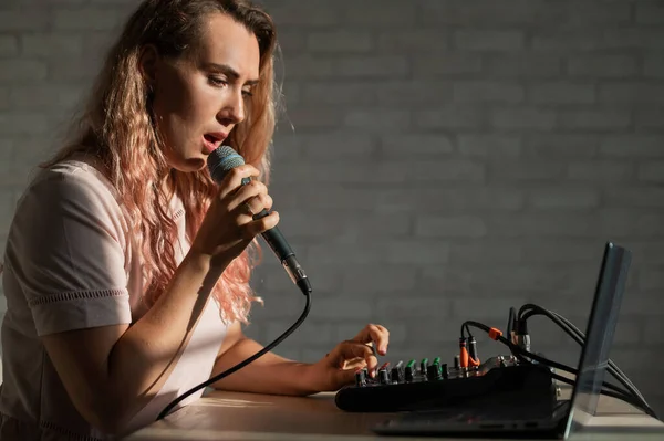 Uma mulher canta em um microfone e joga online. Uma blogueira feminina está gravando uma música usando um sintetizador com um laptop. — Fotografia de Stock