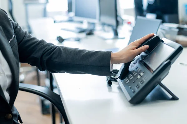 Primer plano mano femenina en el teléfono fijo en la oficina. Mujer sin rostro en un traje trabaja como recepcionista contestando el teléfono a las llamadas de los clientes. — Foto de Stock