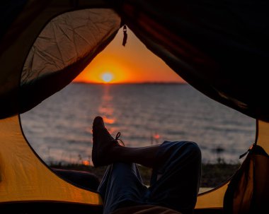 Gün batımında sahilde bir turist çadırında kadın bacakları. Kadın nehir kenarında yürüyüş yapıyor ve kamp yapıyor..