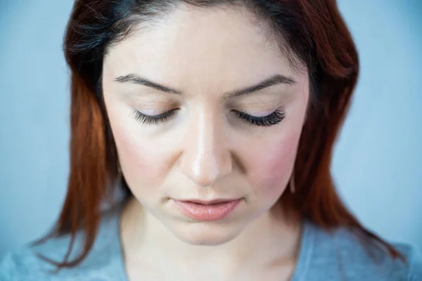 Caucasian woman with extended eyelashes in one eye for comparison. Portrait of a girl before and after artificial eyelash extension procedure.