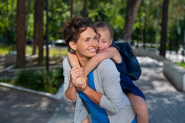 Güzel, beyaz bir kadın kızına arka bahçede sarılıyor. Sırt çantalı bir kız annesine sevgiyle sarılıyor..