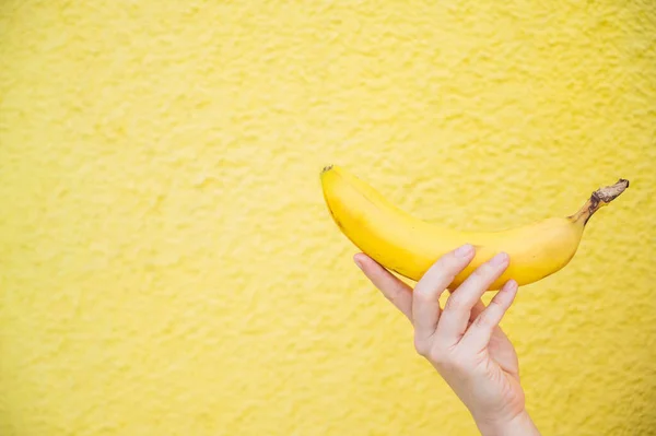 Närbild av en banan i en kvinnlig hand på en gul bakgrund. — Stockfoto