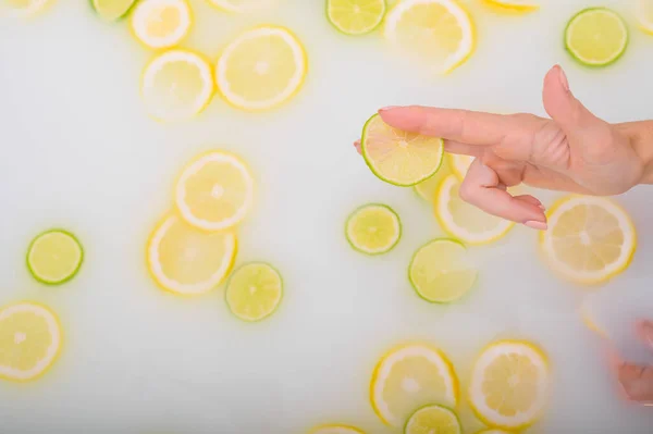 Gros plan d'une main féminine tenant une tranche d'agrumes dans un bain de lait. — Photo