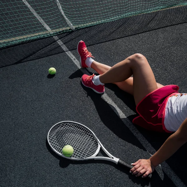 Holka bez tváře ve sportovní sukni sedí na tenisovém kurtu a drží raketu. Pohled shora na ženské nohy. — Stock fotografie