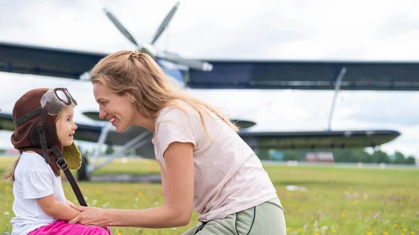 Ein kleines Mädchen im Pilotenkostüm mit ihrer Mutter auf dem Flugplatz. — Stockfoto