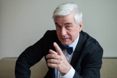 Takım elbiseli yaşlı bir adam parmağını gösterir..