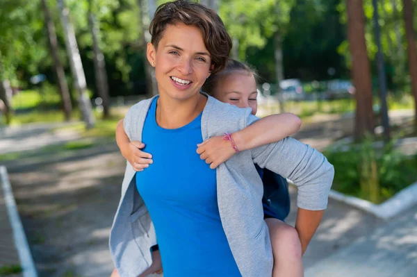 Красивая белая женщина держит свою дочь школьницу на улице. Девушка с рюкзаком с любовью обнимает свою мать сзади. — стоковое фото
