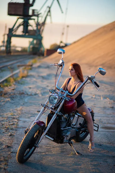 Mulher de cabelos vermelhos em lingerie sexy em salto alto senta-se em uma motocicleta. Atraente menina ruiva senta-se em uma motocicleta ao pôr do sol — Fotografia de Stock