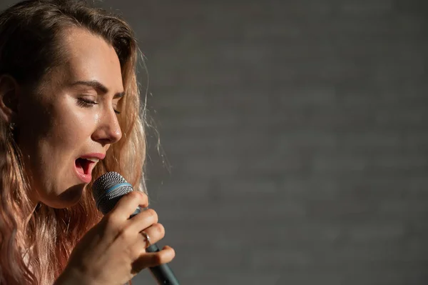 Großaufnahme Porträt einer kaukasischen Frau mit lockigem Haar, die in ein Mikrofon singt. Schöne sinnliche blonde Mädchen singt ein Lied. — Stockfoto