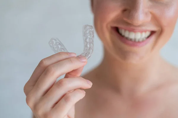 Kadın ellerinde ortodontik silikon şeffaf diş düzenleyicisi var. Elinde çıkartılamaz bir diş teli tutan tanınmayan bir kadın. Diş beyazlatma için bileklik. Mükemmel bir gülümseme. Kesilmiş fotoğraf.