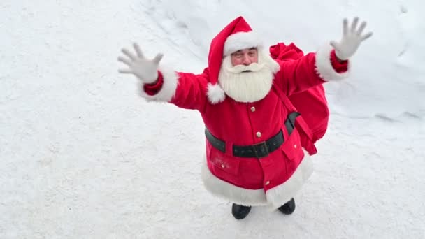 Widok z góry na przyjazny Święty Mikołaj aktywnie gestykulując i życząc Wesołych Świąt. Starszy mężczyzna w stroju Mikołaja stoi na śniegu na zewnątrz i życzy szczęśliwego Nowego Roku. — Wideo stockowe