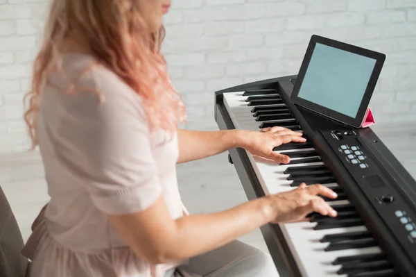 A woman watches video lessons on a digital tablet and plays on an electro synthesizer. The girl learns to play the piano remotely. — Stock Photo, Image