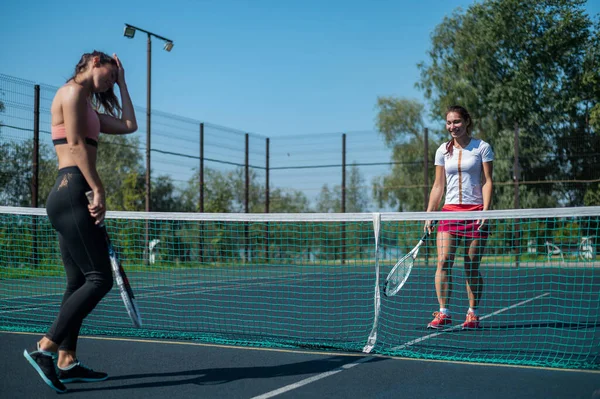 Two athletic young women play tennis on an outdoor court on a hot summer day. The girl defeated her tennis rival. — Stock Photo, Image