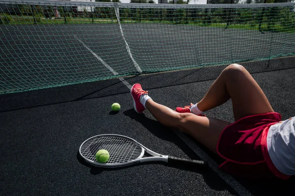 Holka bez tváře ve sportovní sukni sedí na tenisovém kurtu a drží raketu. Pohled shora na ženské nohy. — Stock fotografie