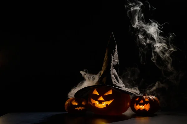 Tres faroles brillan en la oscuridad en medio de la niebla. Calabaza de Halloween en un sombrero de bruja. — Foto de Stock