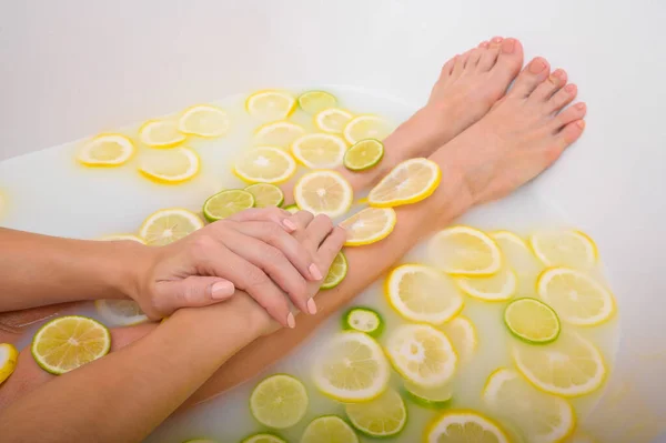 Krásná mladá žena bez tváře se koupe s mléčnými citróny a citrónem. Vystřižená fotka. Detailní záběr ženských rukou a nohou v bělící koupeli. — Stock fotografie
